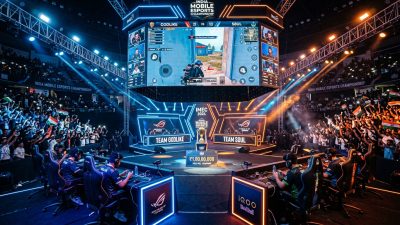 High-energy esports tournament arena with massive screens showing mobile game gameplay