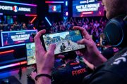 Hands holding smartphone showing battle royale mobile game with gaming setup
