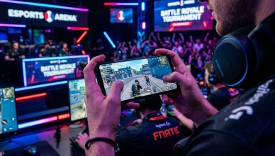 Hands holding smartphone showing battle royale mobile game with gaming setup