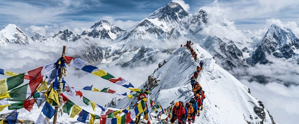 Climbers ascending toward Everest summit with prayer flags and Himalayan panorama