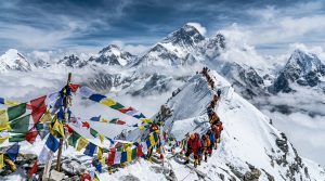 Climbers ascending toward Everest summit with prayer flags and Himalayan panorama