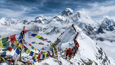Climbers ascending toward Everest summit with prayer flags and Himalayan panorama