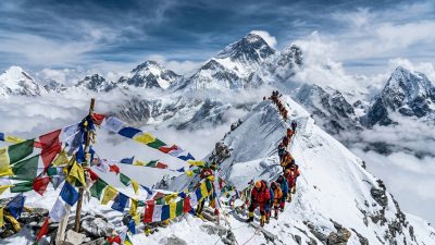 Climbers ascending toward Everest summit with prayer flags and Himalayan panorama