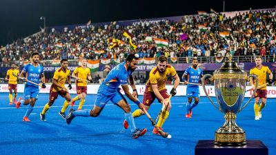 Intense field hockey match in packed Indian stadium with championship trophy
